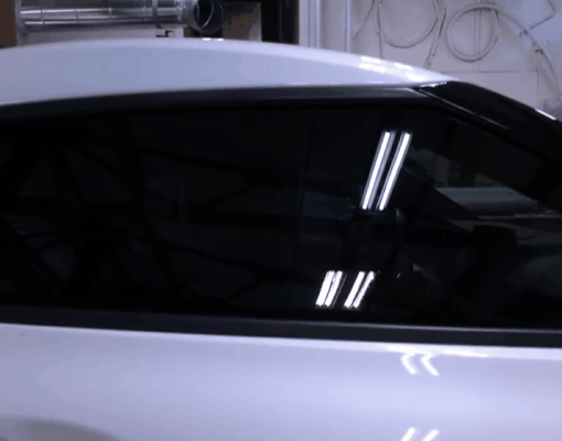 Dark window tint on the side window of a white vehicle inside a shop