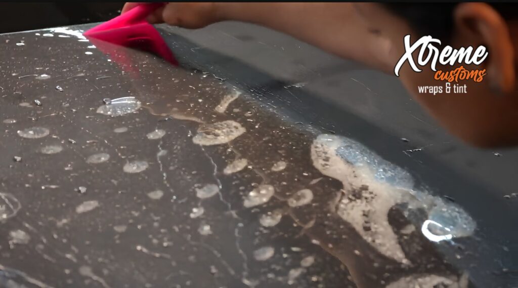 Installer smoothing paint protection film over a wet vehicle panel with a pink squeegee at Xtreme Customs Wraps & Tint