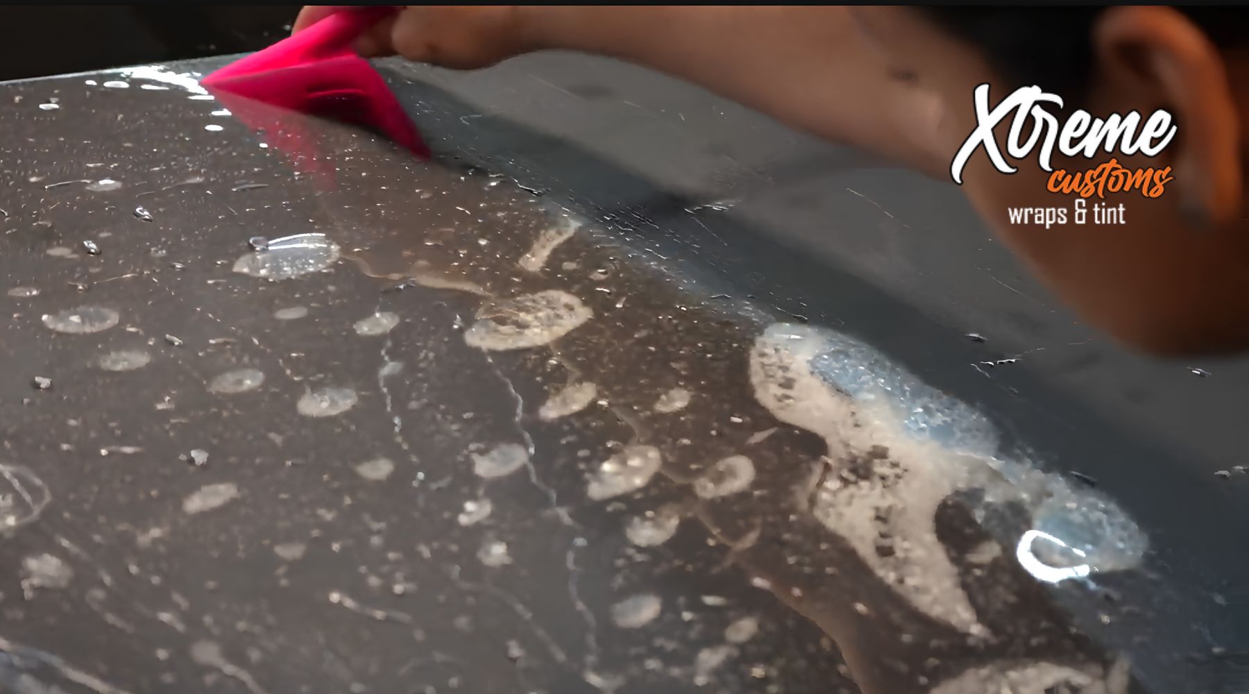 Installer smoothing paint protection film over a wet vehicle panel with a pink squeegee at Xtreme Customs Wraps & Tint