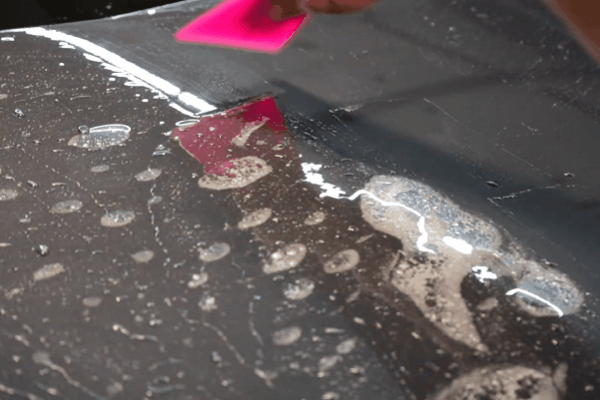 Installer smoothing paint protection film over a wet vehicle panel with a squeegee